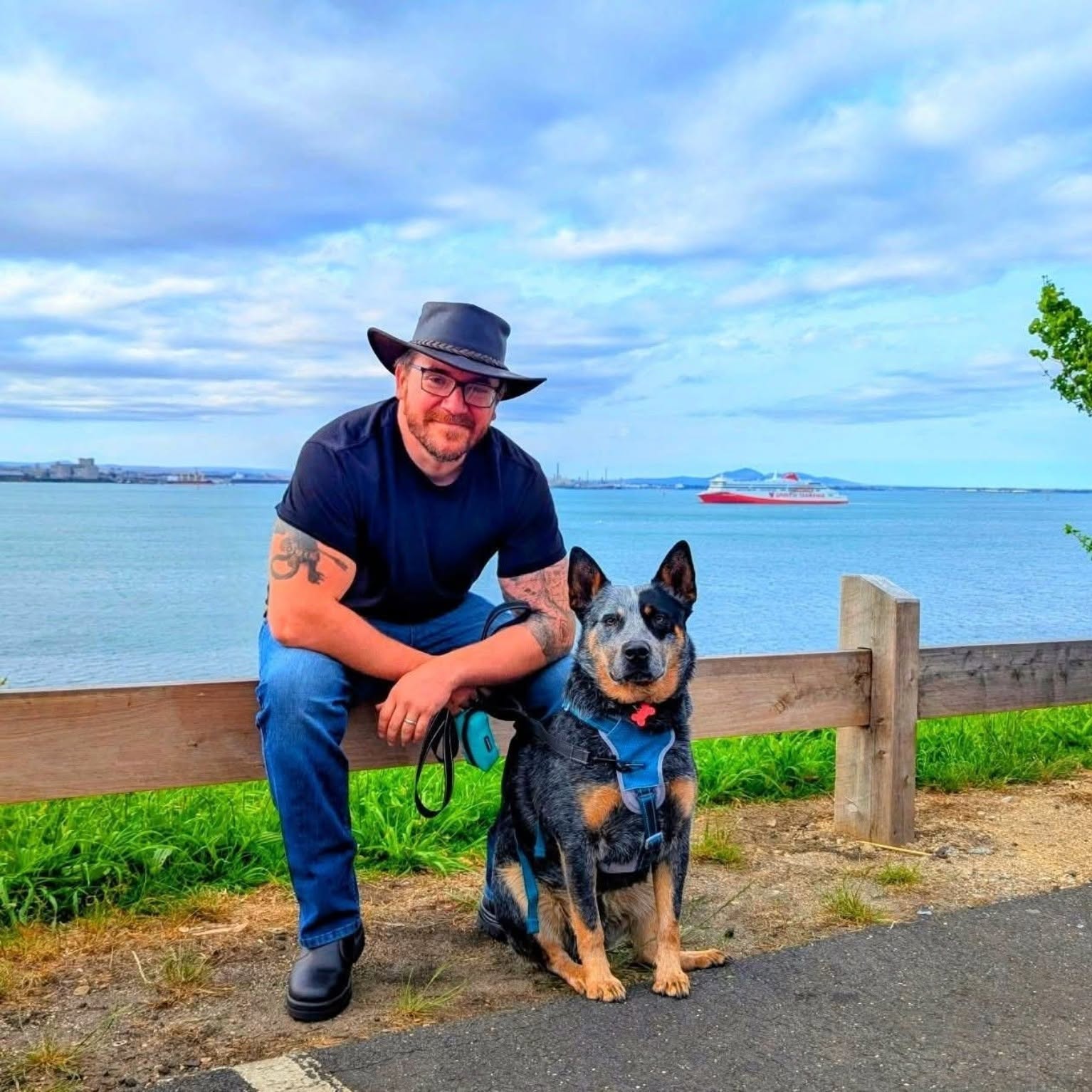 Ben sitting on a fence by the bay with a blue heeler beside him