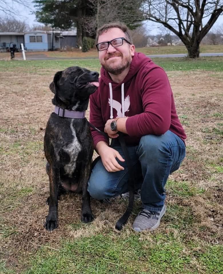 Ben crouching beside a large black dog, both looking at the camera