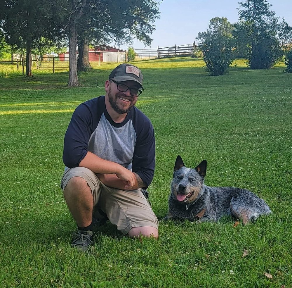 Ben crouching in a field beside a cattle dog