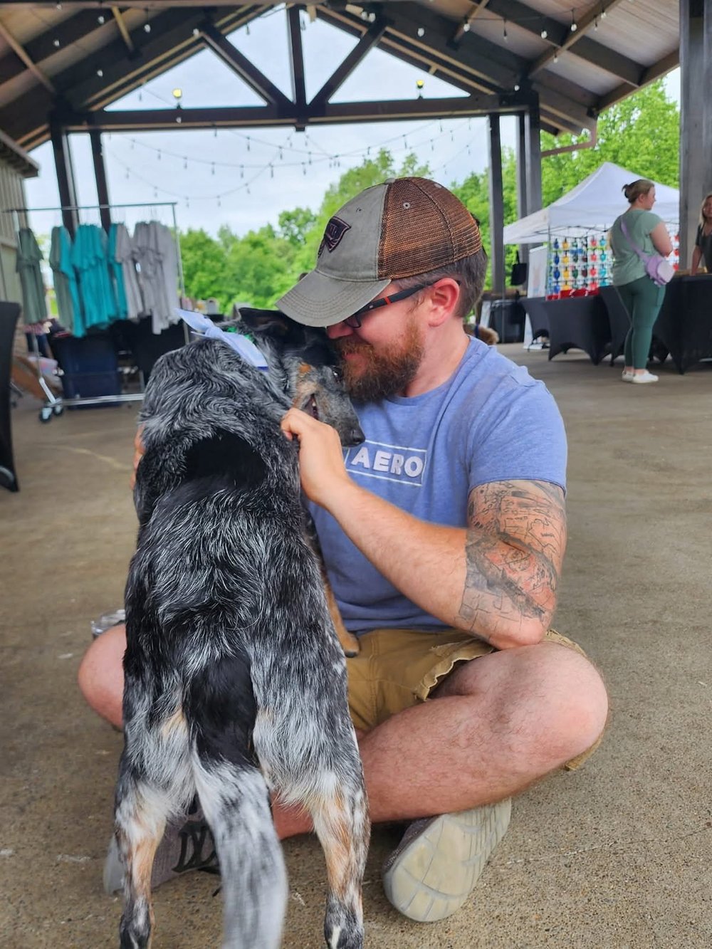 Ben sitting on the ground face to face with a speckled dog