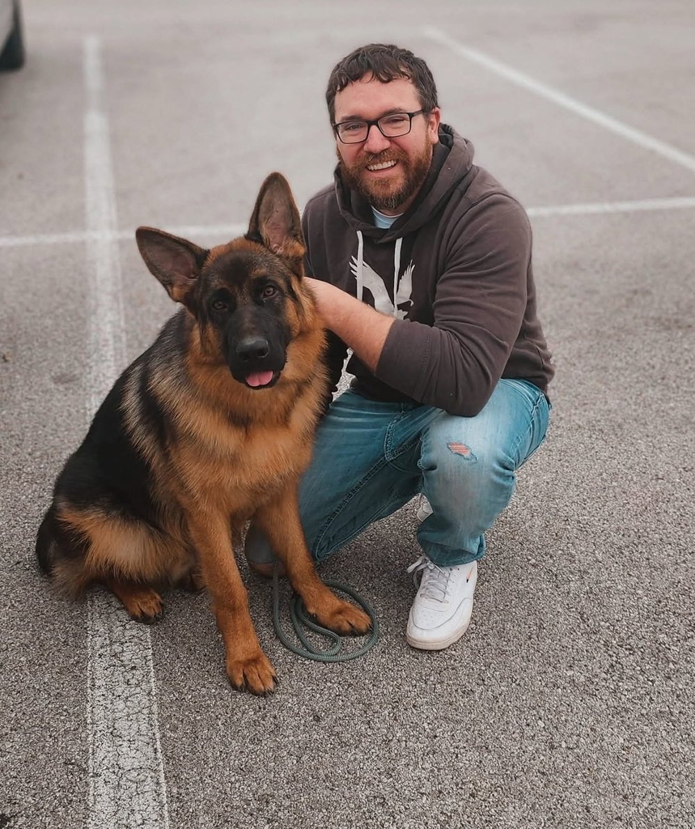 Ben kneeling with his arm around a German shepherd